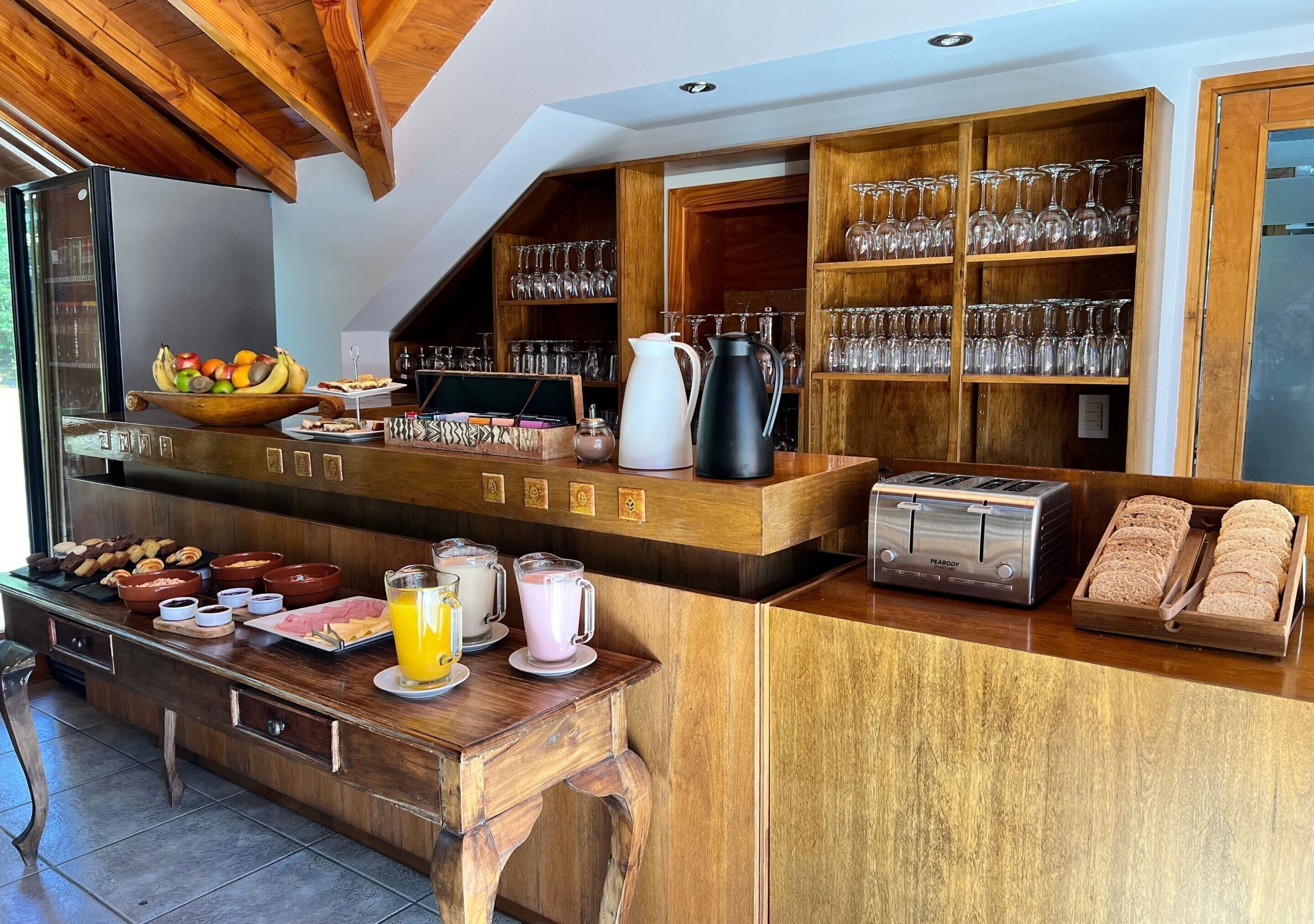 Un banco della colazione con una varietà di cibi, tra cui frutta, dolci e bevande. Si vedono anche scaffali con bicchieri e un tostapane.