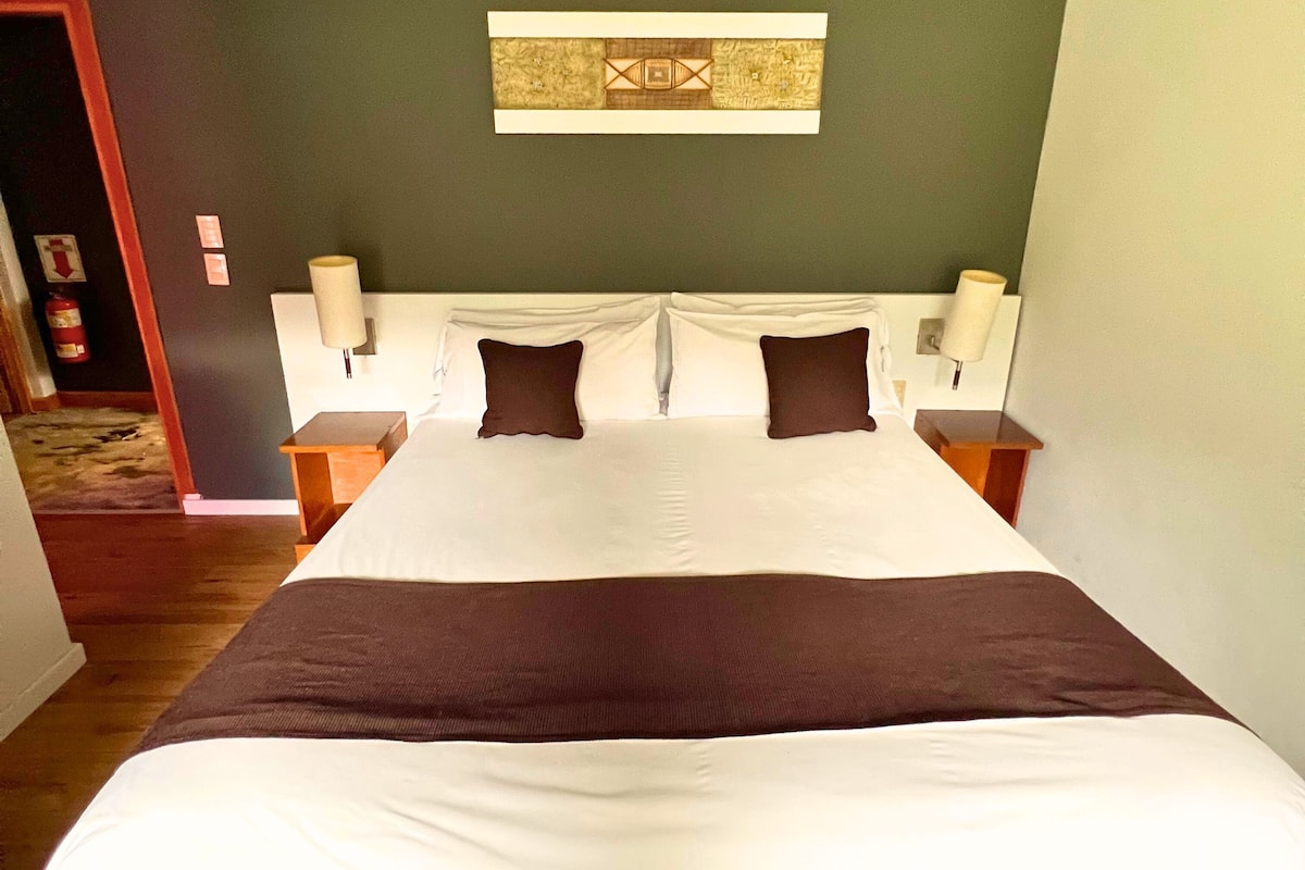 A hotel room with a large bed, two nightstands, a wall-mounted lamp, and a decorative wall piece.