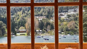 A view from a wooden-framed window overlooking a lake with boats, surrounded by trees and buildings. - El Muelle by DOT Boutique (Villa La Angostura)