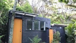 En liten, envåningsbyggnad med en svart och orange fasad, omgiven av frodig grönska.