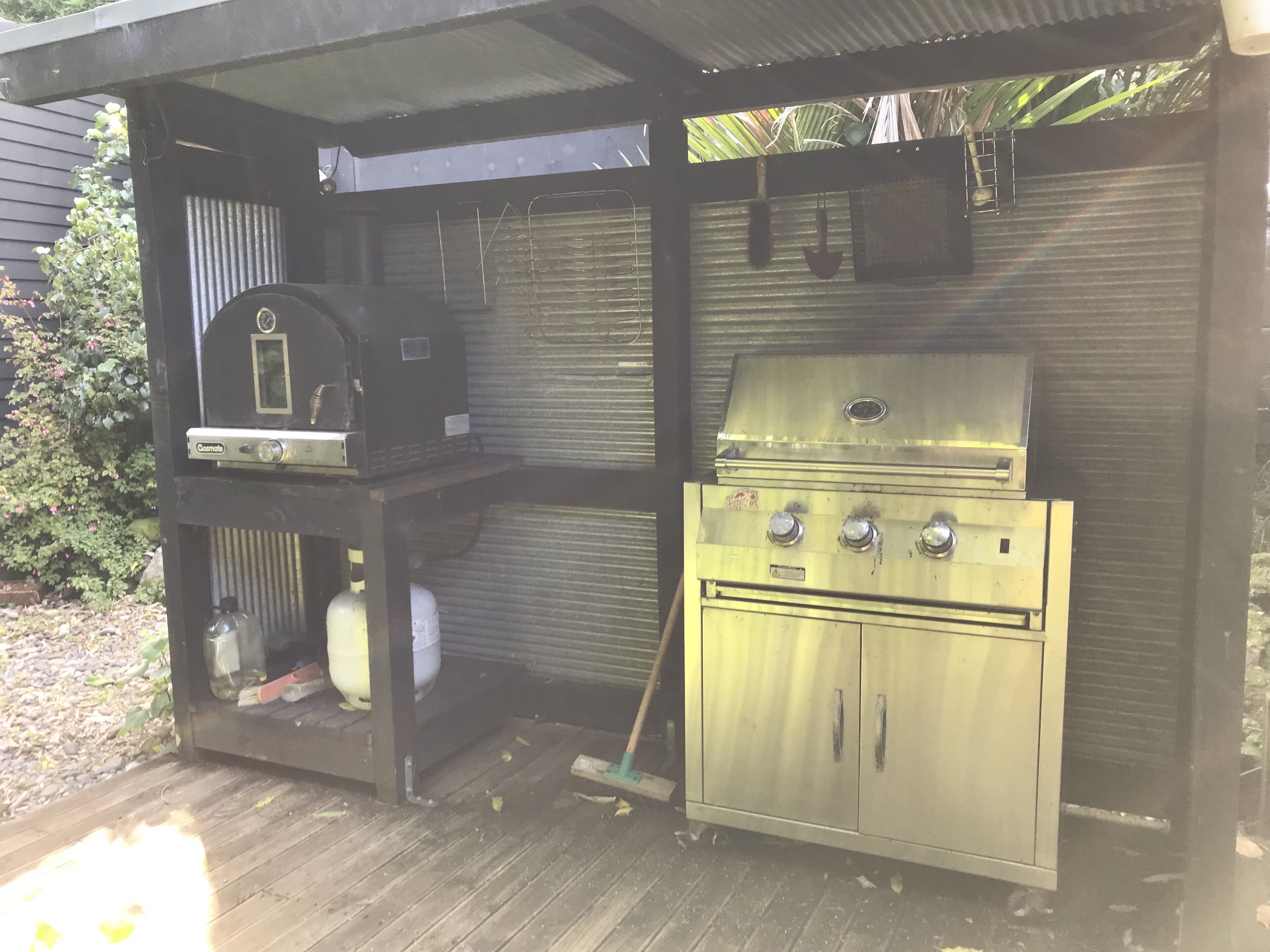 Ett takförsett utomhusområde med grillplats, utrustat med en gasolgrill och en kolgrill.