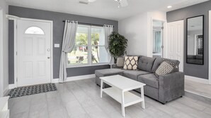 A modern living room with a grey sectional sofa, a white coffee table, a ceiling fan, and a large window with curtains. - House in Melbourne With Pool (Melbourne)