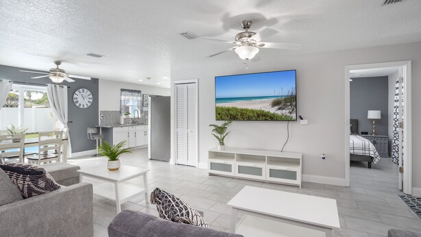 A modern living room with a large TV, ceiling fans, and a view of the beach through the window. - House in Melbourne With Pool (Melbourne)