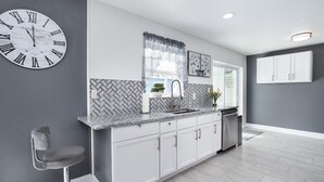 A modern kitchen with a marble countertop, white cabinets, and a large wall clock. - House in Melbourne With Pool (Melbourne)