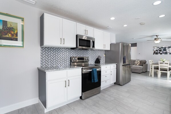 A modern kitchen with white cabinets, stainless steel appliances, and a herringbone tile backsplash. - House in Melbourne With Pool (Melbourne)