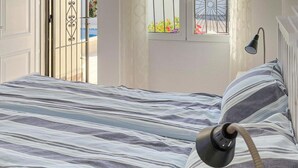 A bed with striped bedding, a bedside lamp, and a window with a view of a balcony and flowers.