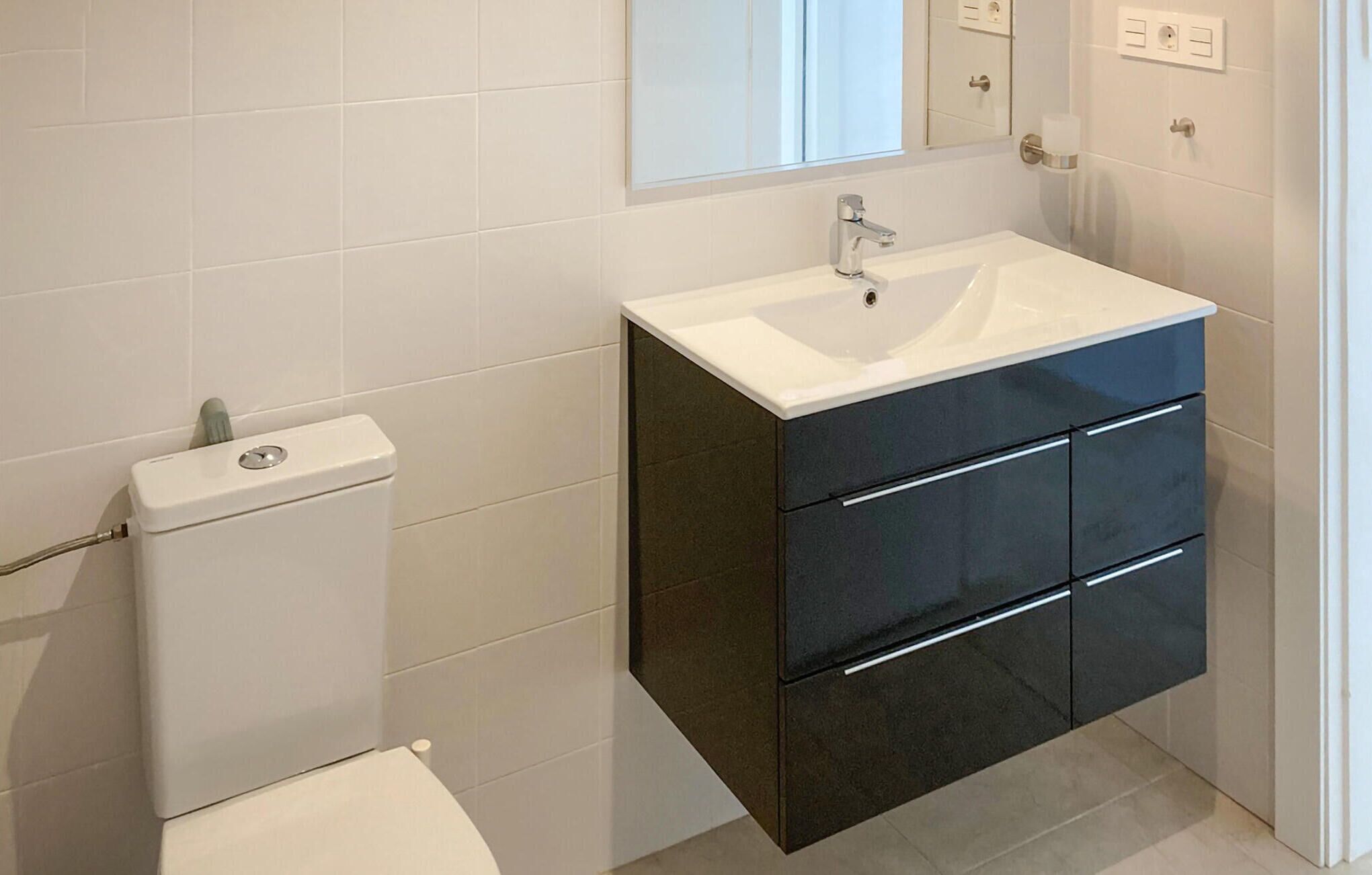 A bathroom with a white toilet, a black vanity with a white sink, and a mirror above the sink.