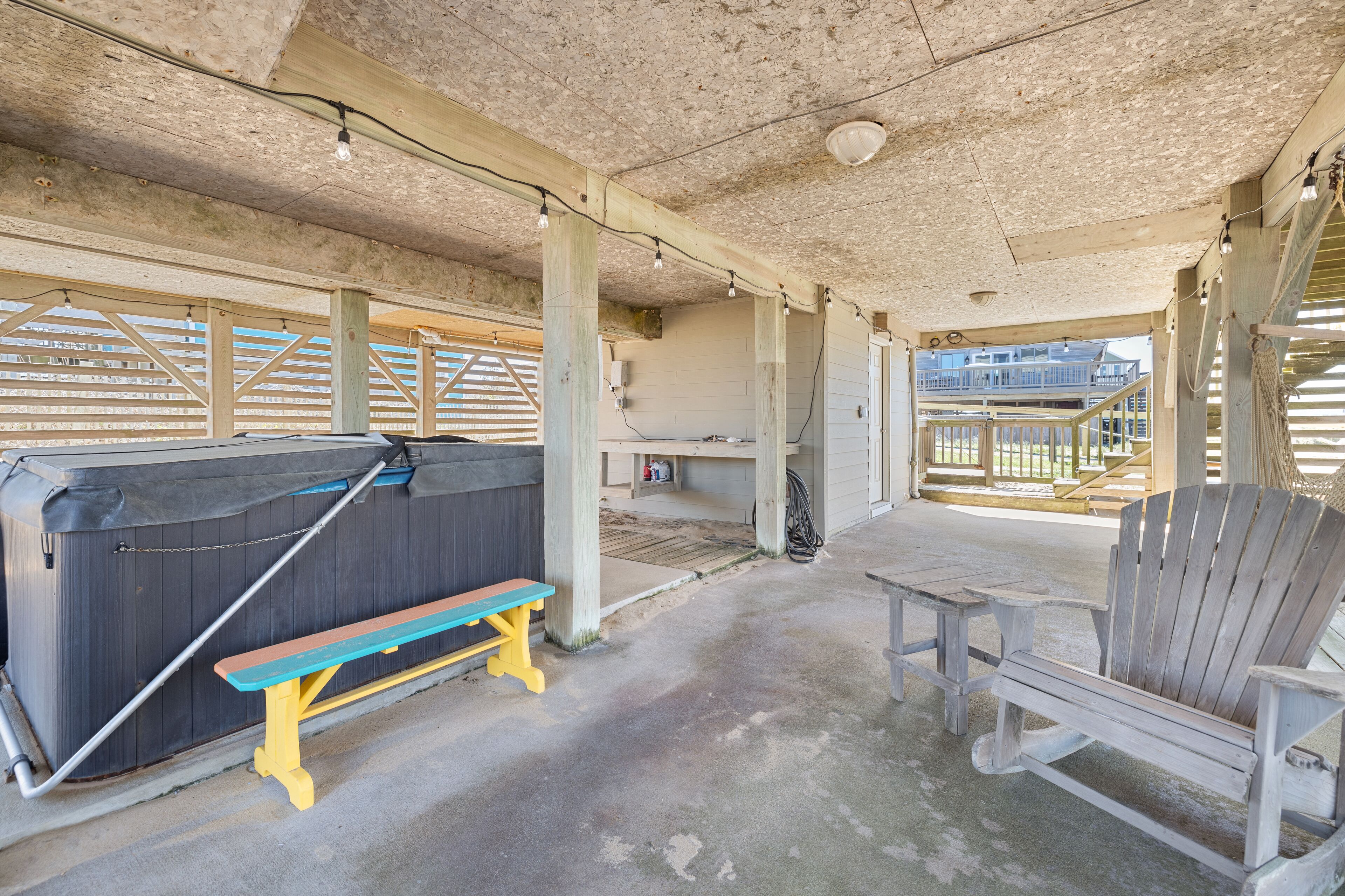 Une terrasse extérieure couverte, équipée d’un jacuzzi, de bancs en bois et d’une chaise en bois.
