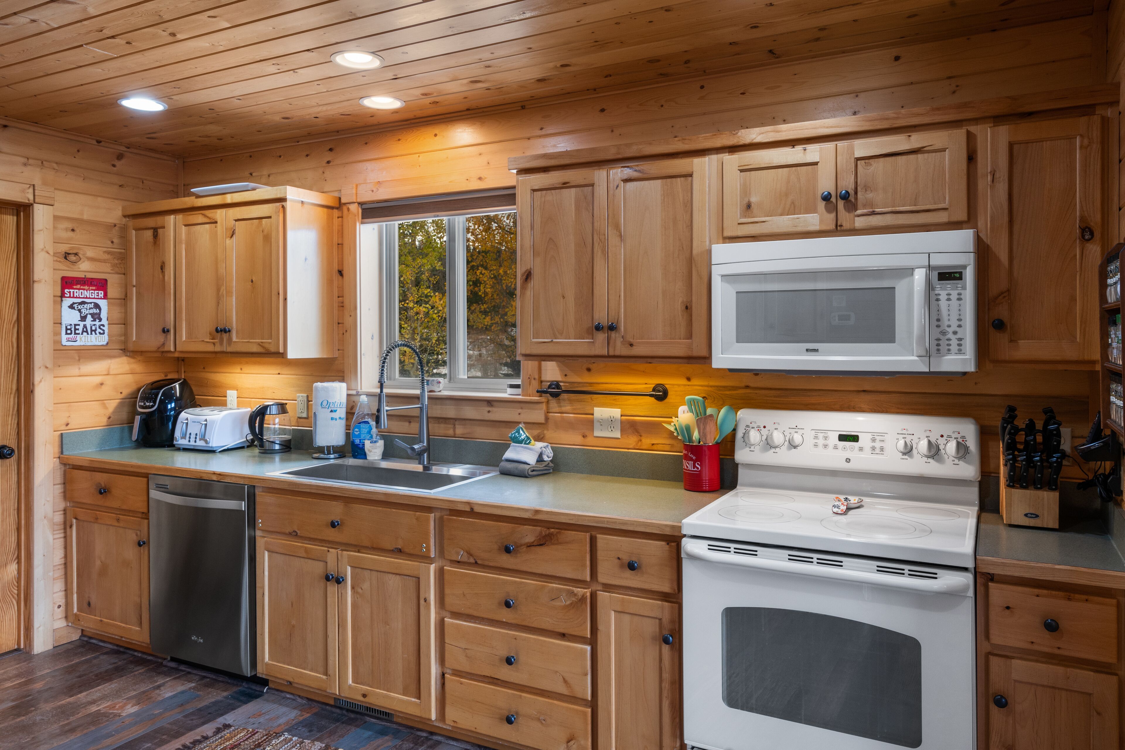 Una cocina estilo cabaña de madera con lavavajillas, microondas, estufa y armarios de madera.