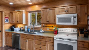 Una cocina estilo cabaña de madera con lavavajillas, microondas, estufa y armarios de madera.