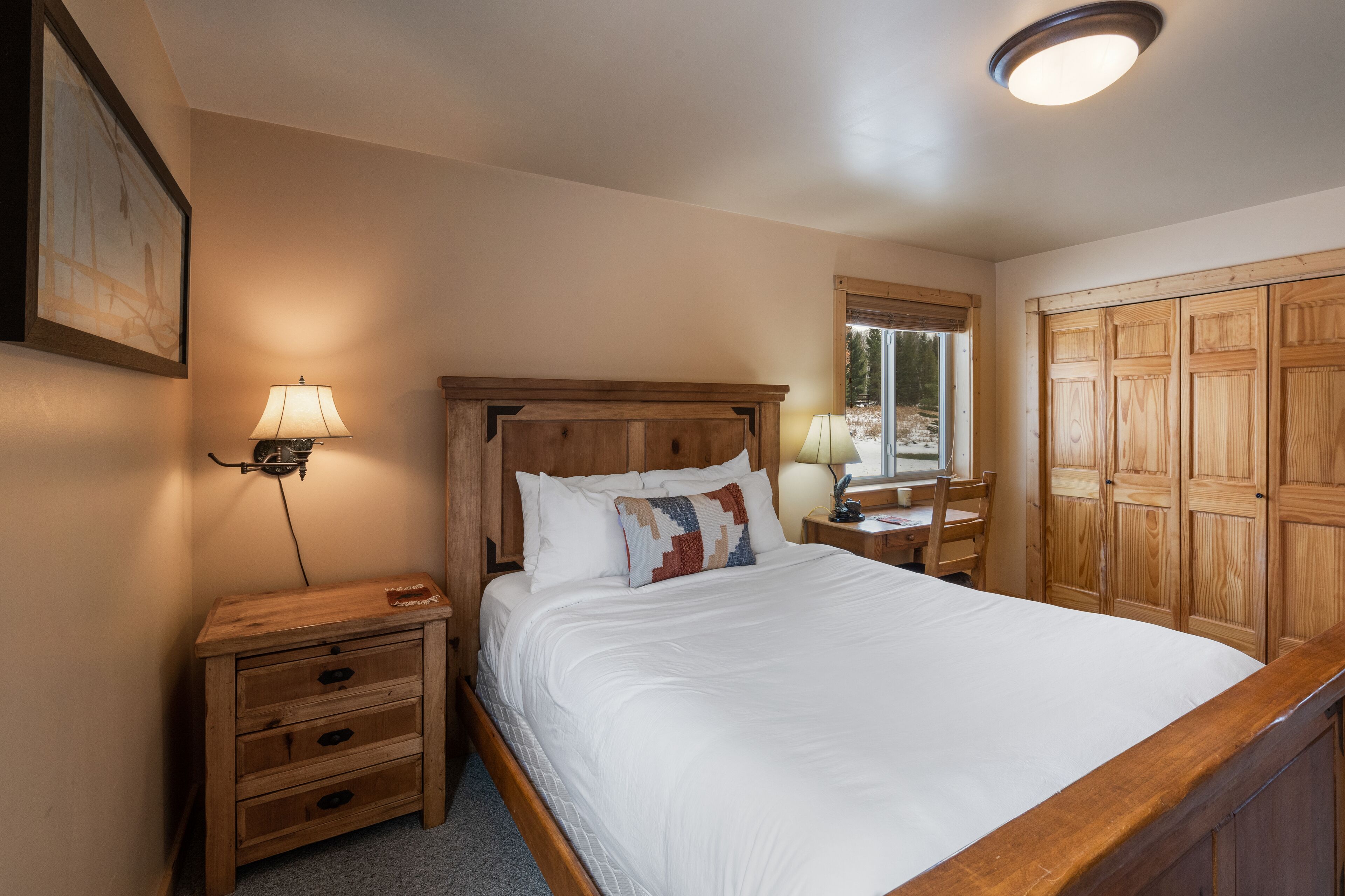 A bedroom with a wooden bed, bedside tables, a nightstand, a window, and a wardrobe.