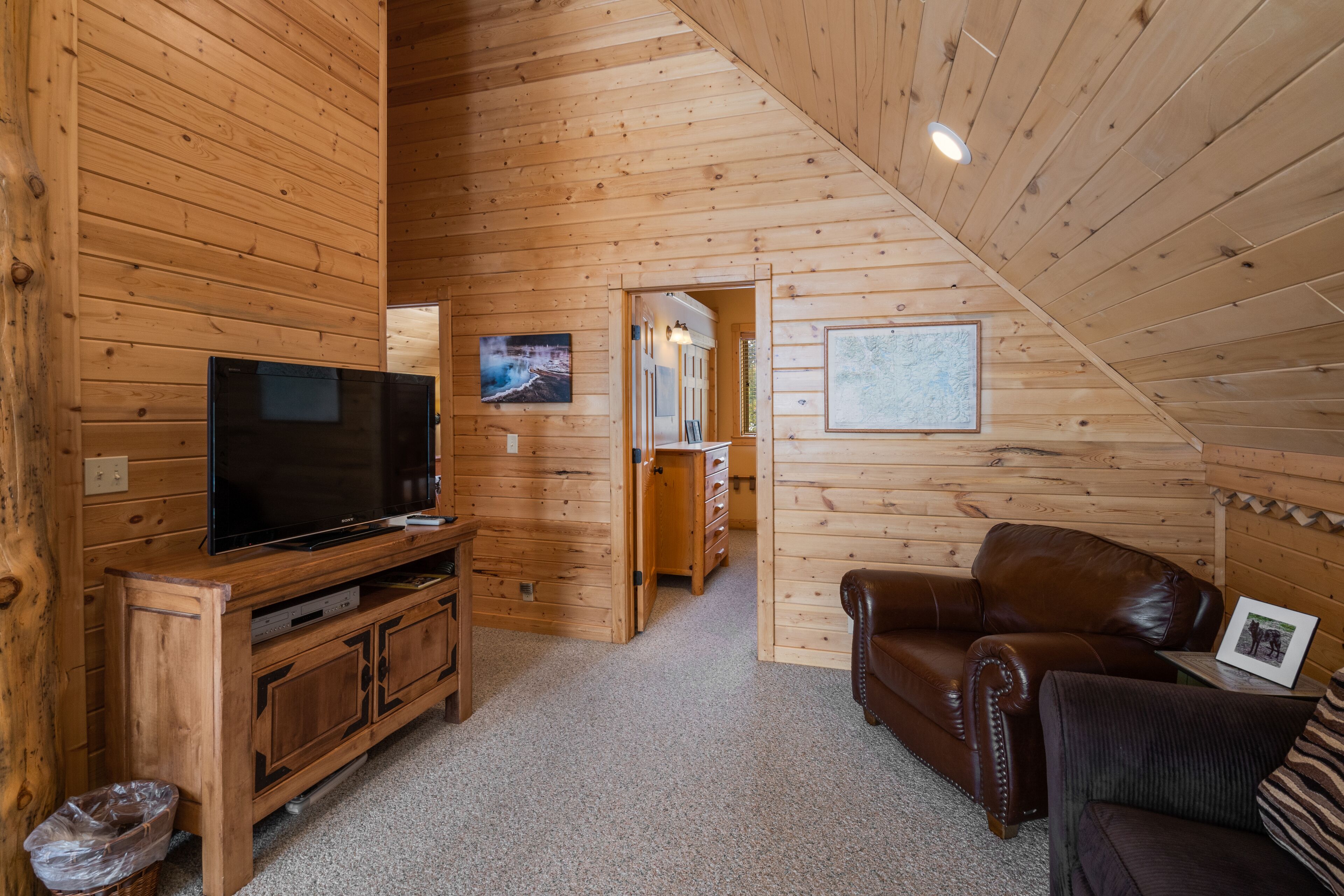 Ein Holzinterieur mit einem Fernseher auf einem Holzständer, einem Ledersofa und einem gerahmten Bild an der Wand.