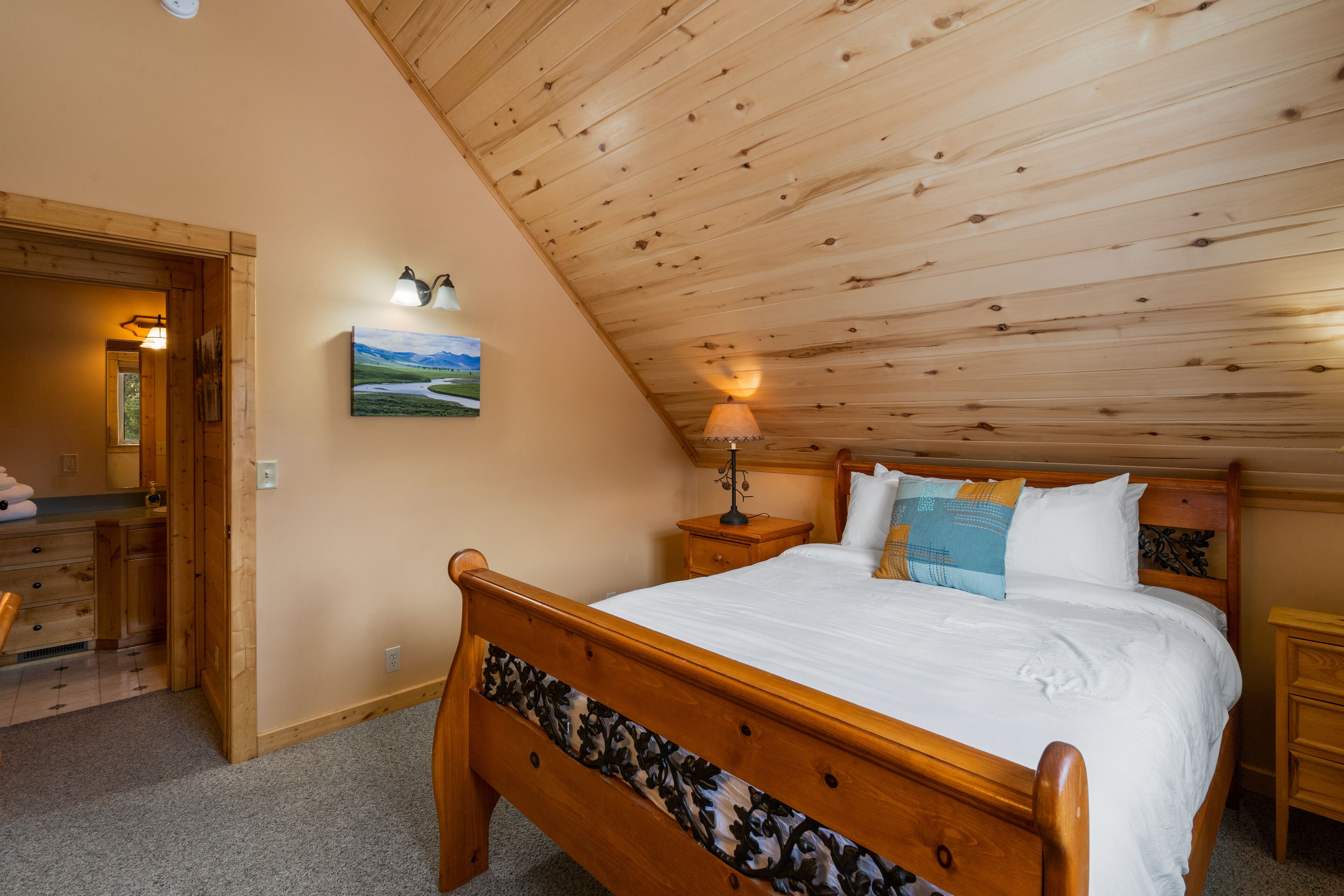 Une chambre avec un plafond en bois, un lit avec une literie blanche, une table de chevet avec une lampe et un tableau au mur.