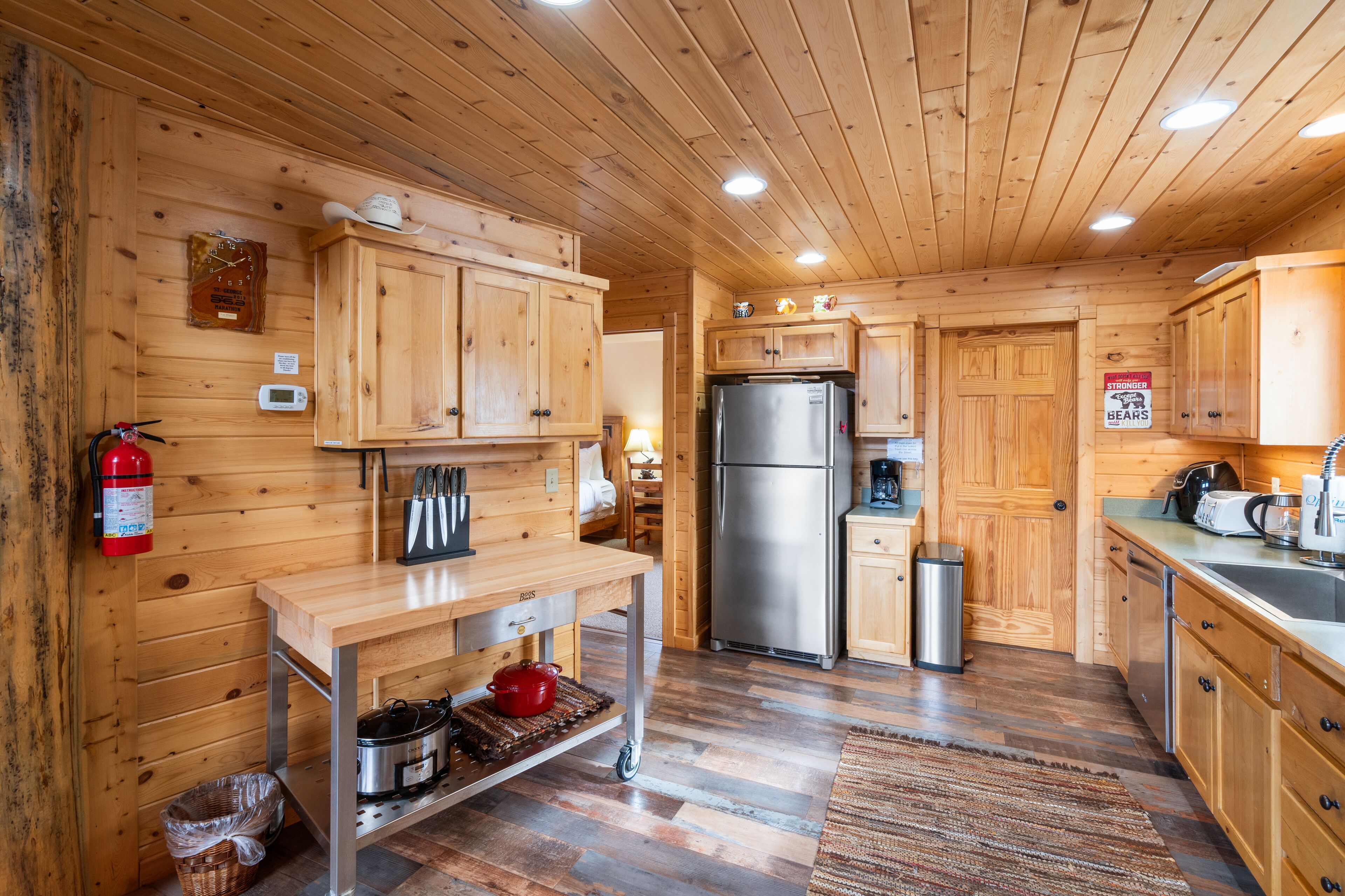 Interior de una cabaña de madera con cocina, que incluye armarios de madera, un refrigerador de acero inoxidable, una cafetera y un lavamanos.