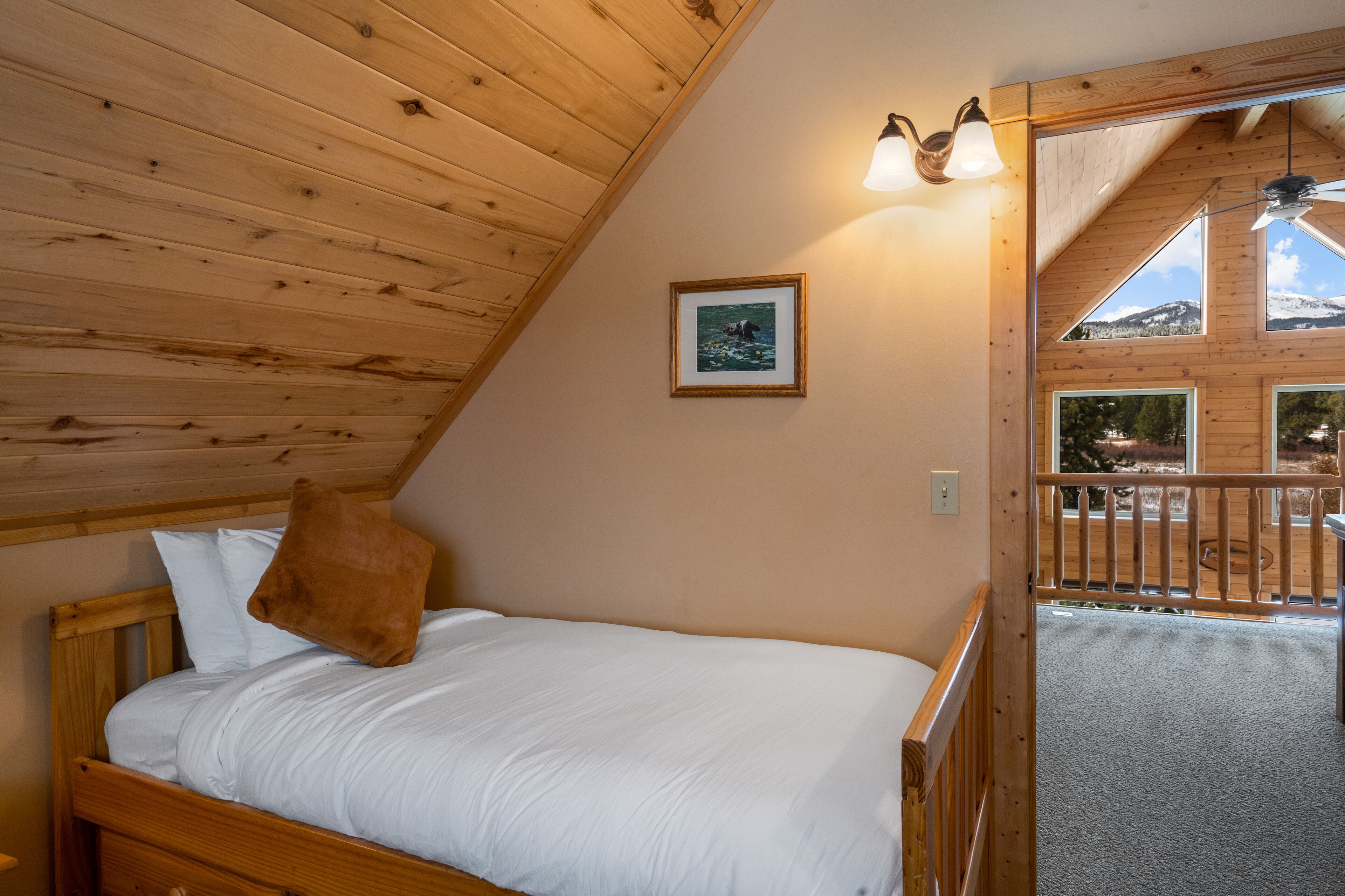 A wooden-paneled bedroom with a bed, a framed picture, and a balcony with a view of the mountains.