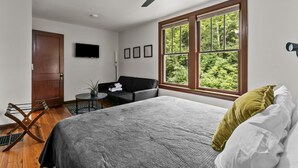 A bedroom with a bed, a ceiling fan, a window with a view of greenery, a door, and a flat-screen TV on the wall. - Historic Hidden Gem - Downtown Southern Pines (Southern Pines)