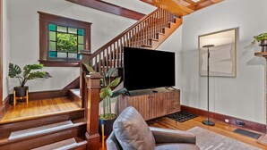 A staircase with wooden railings, a flat-screen TV on a wooden cabinet, a potted plant, and a framed artwork on the wall. - Historic Hidden Gem - Downtown Southern Pines (Southern Pines)