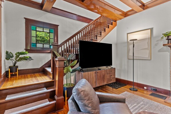 Relax in the living area with a flat-screen TV, comfortable sofa, and a floor lamp, surrounded by a view of lush greenery.