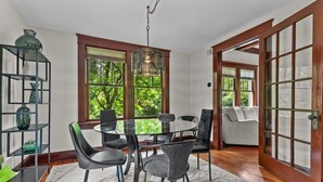 A dining area with a glass table, black and gray chairs, a hanging light fixture, and a view of greenery through large windows. - Historic Hidden Gem - Downtown Southern Pines (Southern Pines)