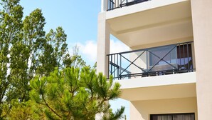 Ein modernes, zweistöckiges Gebäude mit einem Balkon im oberen Bereich, einer Terrasse mit Gartenmöbeln und einem gepflegten Rasen mit Bäumen.