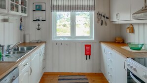 Cocina compacta con armarios blancos, encimera de madera, ventana con cortina a rayas y vistas a zonas verdes.