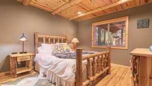 Un dormitorio con un cabecero de madera, una mesita de noche con lámpara, una ventana con persianas y un pequeño armario de madera.