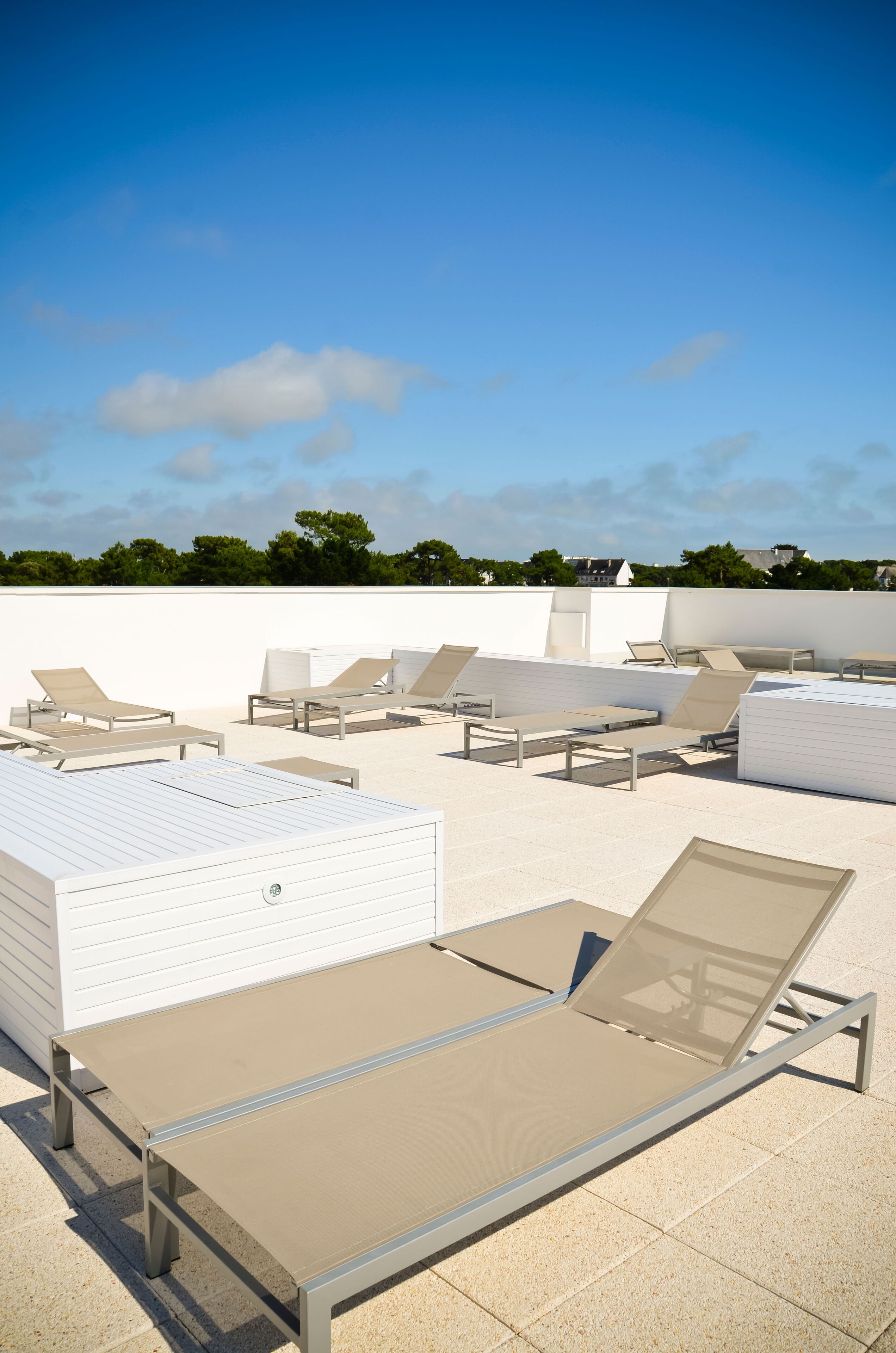 Un espace de détente aménagé sur le toit, avec plusieurs chaises longues et un bâtiment blanc en arrière-plan.