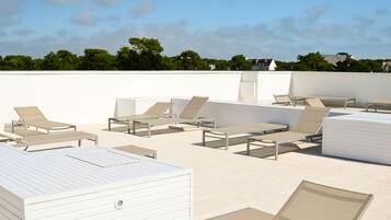 Un espace de détente aménagé sur le toit, avec plusieurs chaises longues et un bâtiment blanc en arrière-plan.