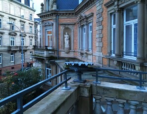 Ein historisches Gebäude mit klassischer Architektur, das eine markante Statue, große Fenster und einen Balkon mit Metallgeländer zeigt.