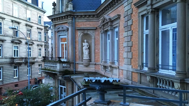 Een historisch gebouw met klassieke architectuur, met een opvallend standbeeld, grote ramen en een balkon met een metalen hekwerk.