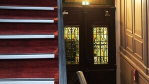 A staircase with red carpeted steps leading to a landing with a door and a light fixture.