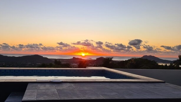 Une piscine sur le toit offrant une vue sur le coucher de soleil, un panneau d’avertissement et une chaîne de montagnes lointaine.