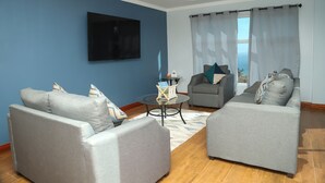 Un salon avec deux canapés gris, une table basse et un téléviseur à écran plat fixé sur un mur bleu.