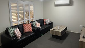 Una sala de estar moderna con un sofá de cuero negro, una mesa de centro de madera y un ventilador de techo.