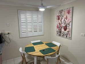 A dining area with a round wooden table, four white chairs, and green placemats.