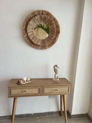 A wooden console table with a woven basket and a seahorse decoration, a woven wall hanging with a plant, and a white wall. - Charming Apartment On The Octopus Beach With Pool (Punta Hermosa)