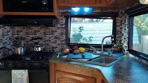 Cocina compacta con estufa, pileta y ventana con vista a un estacionamiento.