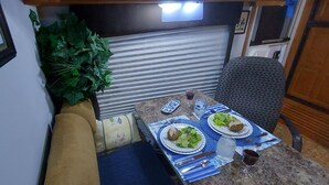 Una kitchenette compacta con una mesa de comedor lista para dos personas, mostrando platos de comida, cubiertos y una copa de vino tinto.