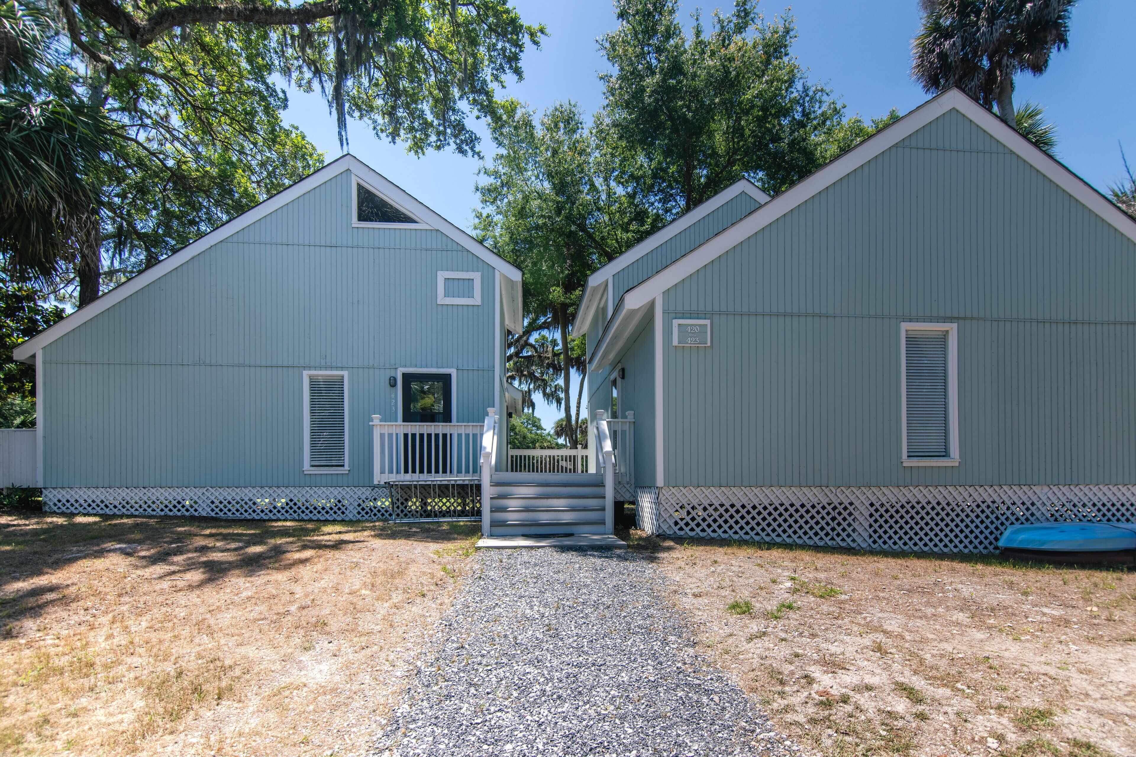 Two blue buildings with white railings and a gravel path leading to a set of stairs.