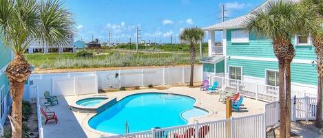 A swimming pool with a white fence, surrounded by palm trees and a house with teal siding.