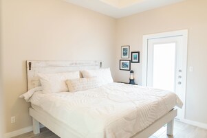 Un dormitorio con una cama blanca, cabecera blanca y una puerta con lámpara.