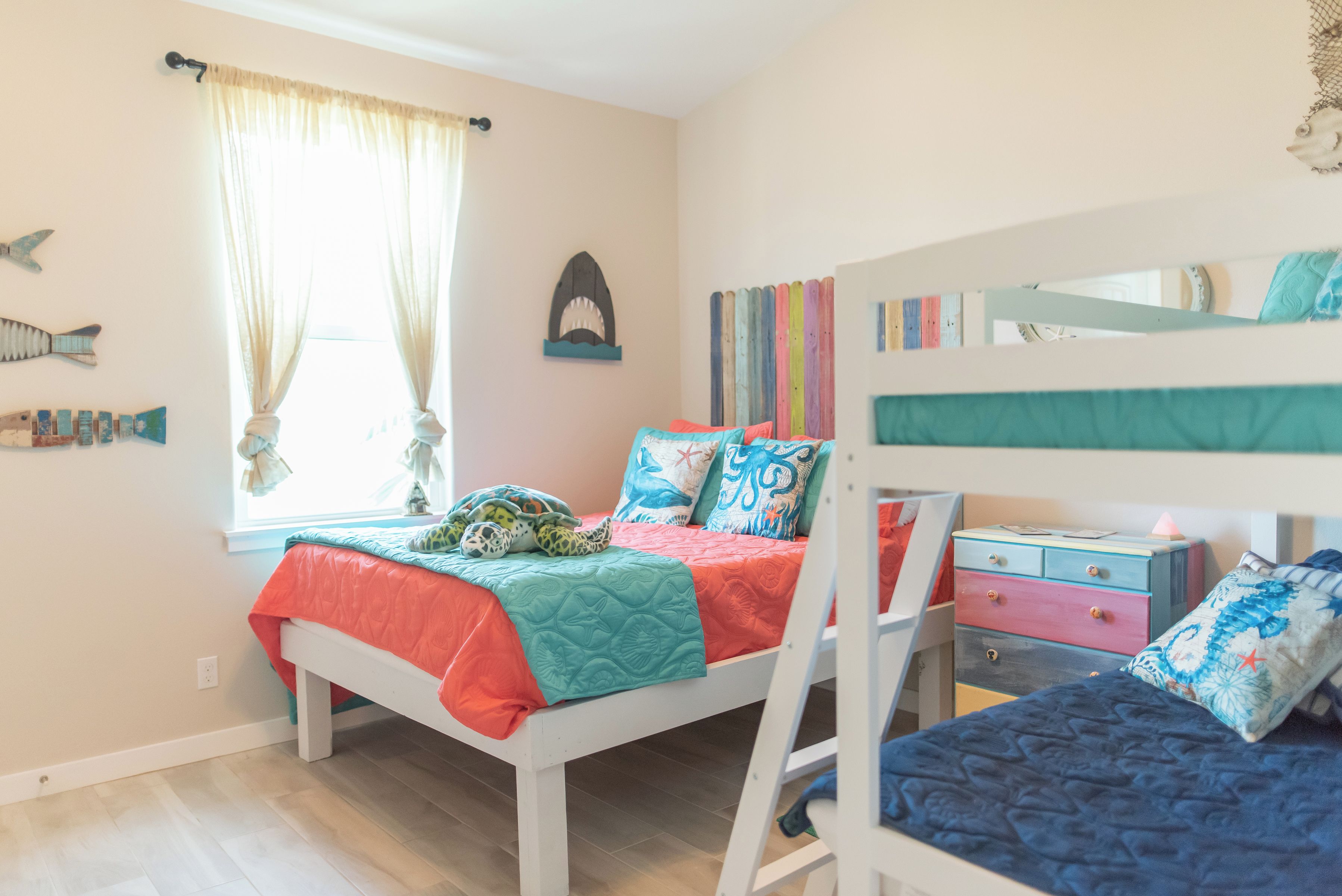 Een kinderkamer met stapelbedden, een raam met gordijnen en decoratie aan de muur.