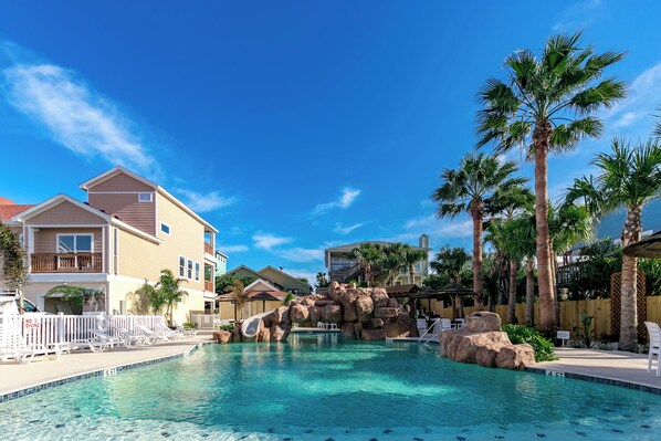 A swimming pool with a rock waterfall, palm trees, and a view of nearby houses. - Soulshine by Silver Sands Vacation Rentals (Port Aransas)