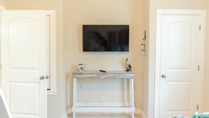 Una habitació amb una porta blanca, un taulell de truc blanc amb un quadre, i un llit amb un llençol de llit estampat en blau i blanc.