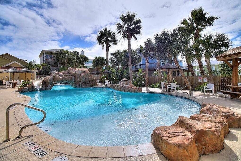 Une piscine agrémentée d’un élément rocheux, entourée de palmiers et de chaises longues.