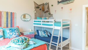 Habitació infantil amb lliteres, un taulell, un mirall i decoracions murals.