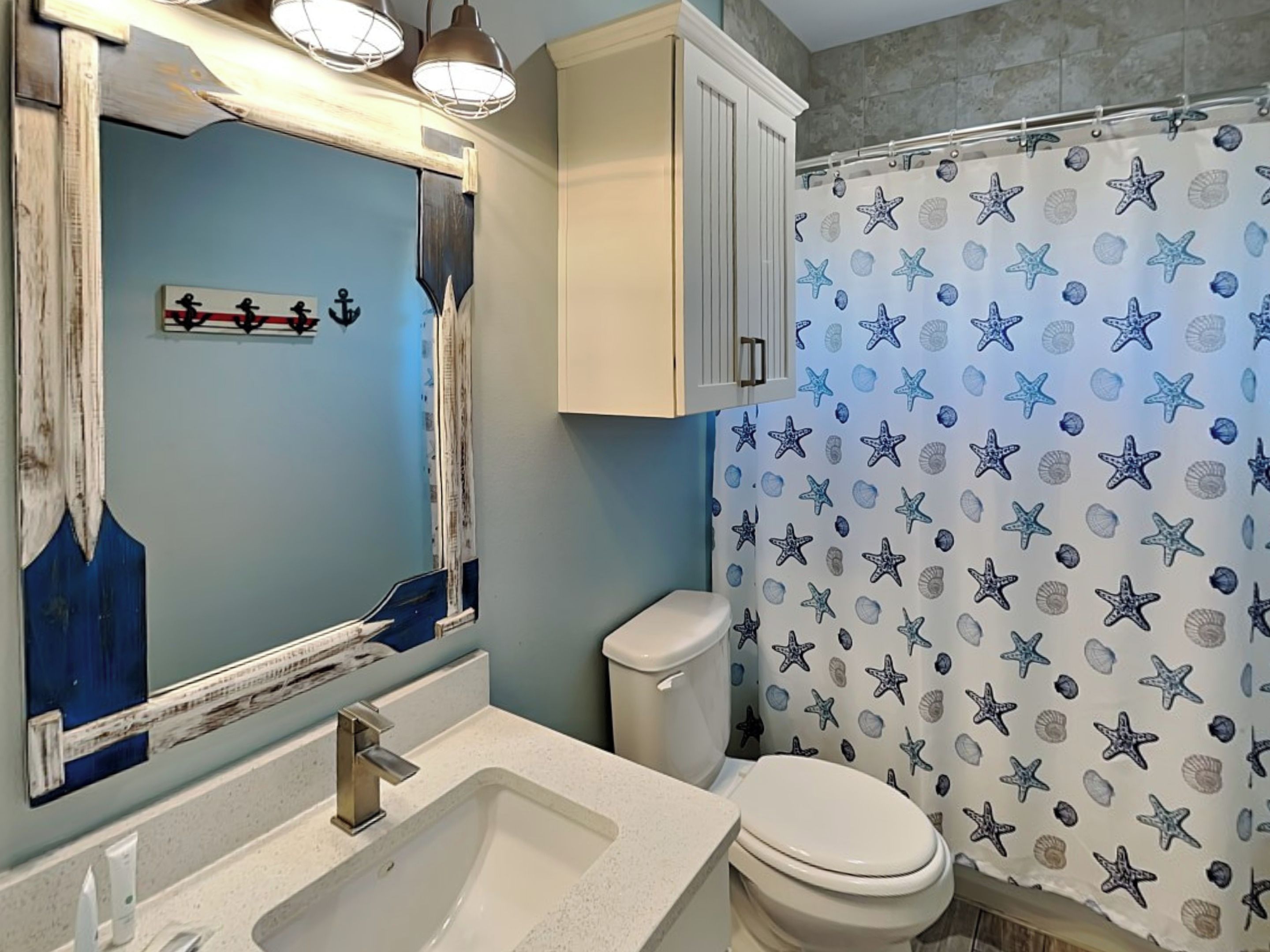 A bathroom with a blue wall, a white sink, a toilet, and a shower curtain with starfish and seashells.