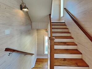Uma escada de madeira com corrimão, uma luminária acima e uma janela no topo.