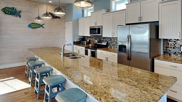 A modern kitchen with a granite countertop, stainless steel appliances, and blue bar stools. - Turtle Paradise by Silver Sands Vacation Rentals (Port Aransas)