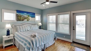 A bedroom with a bed, nightstands, a ceiling fan, and a door with a view. - Turtle Paradise by Silver Sands Vacation Rentals (Port Aransas)